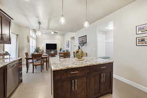 Kitchen with dark wood finish cabinets, dishwasher, light stone countertops, hanging light fixtures, and a ceiling fan