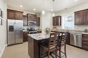Kitchen with stainless steel appliances, light stone counters, dark wood finish cabinetry, a kitchen island, and a breakfast bar