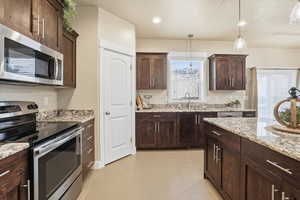 Kitchen featuring stainless steel appliances, dark wood finish cabinets, and light stone counters