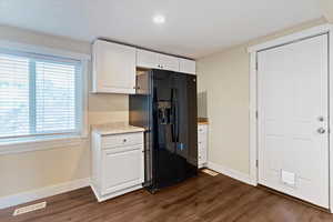 Kitchen with black refrigerator with ice dispenser, white cabinetry, and dark wood-style flooring