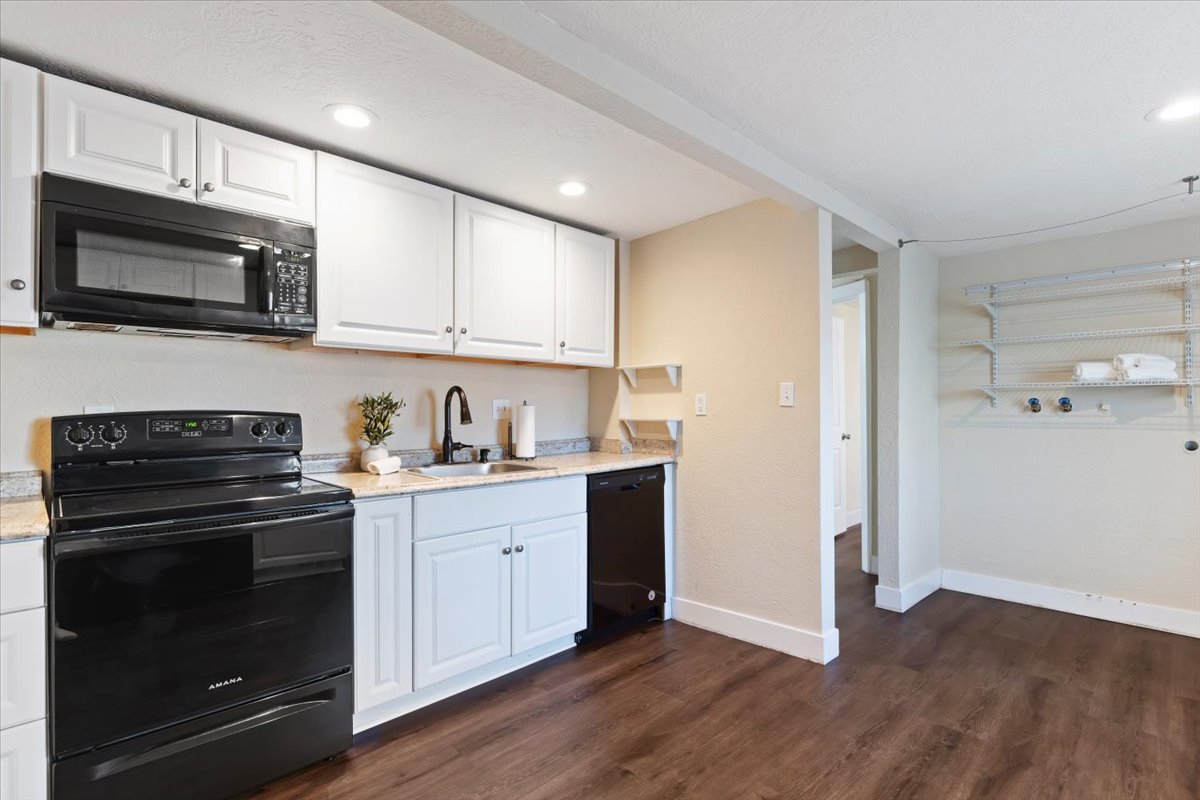 Kitchen featuring black appliances, white cabinets, dark wood-style flooring, light stone countertops, and recessed lighting