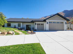 View of front of property with an attached garage, concrete driveway, a front lawn, a shingled roof, and a mountain view