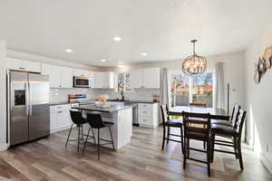 Kitchen with stainless steel appliances, white cabinets, a kitchen bar, a kitchen island, and suspended lighting