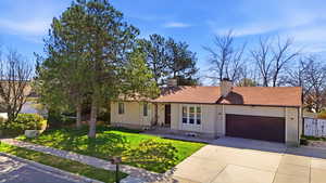 Ranch-style home featuring an attached garage, driveway, a front lawn, and a chimney