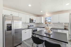Kitchen featuring stainless steel appliances, light wood-style floors, white cabinets, a kitchen breakfast bar, and recessed lighting