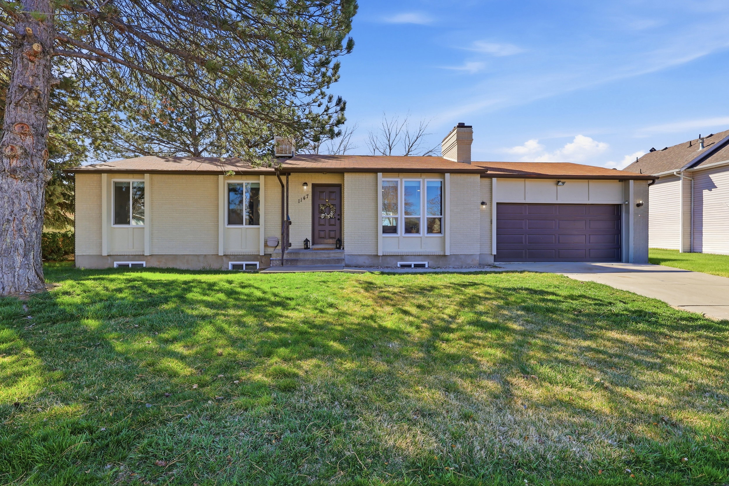 Ranch-style house with brick siding, a chimney, an attached garage, driveway, and a front yard