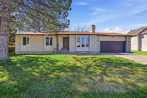 Ranch-style house with brick siding, a chimney, an attached garage, driveway, and a front yard