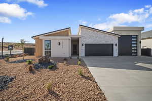 View of front of property featuring a garage, driveway, stone siding, and stucco siding
