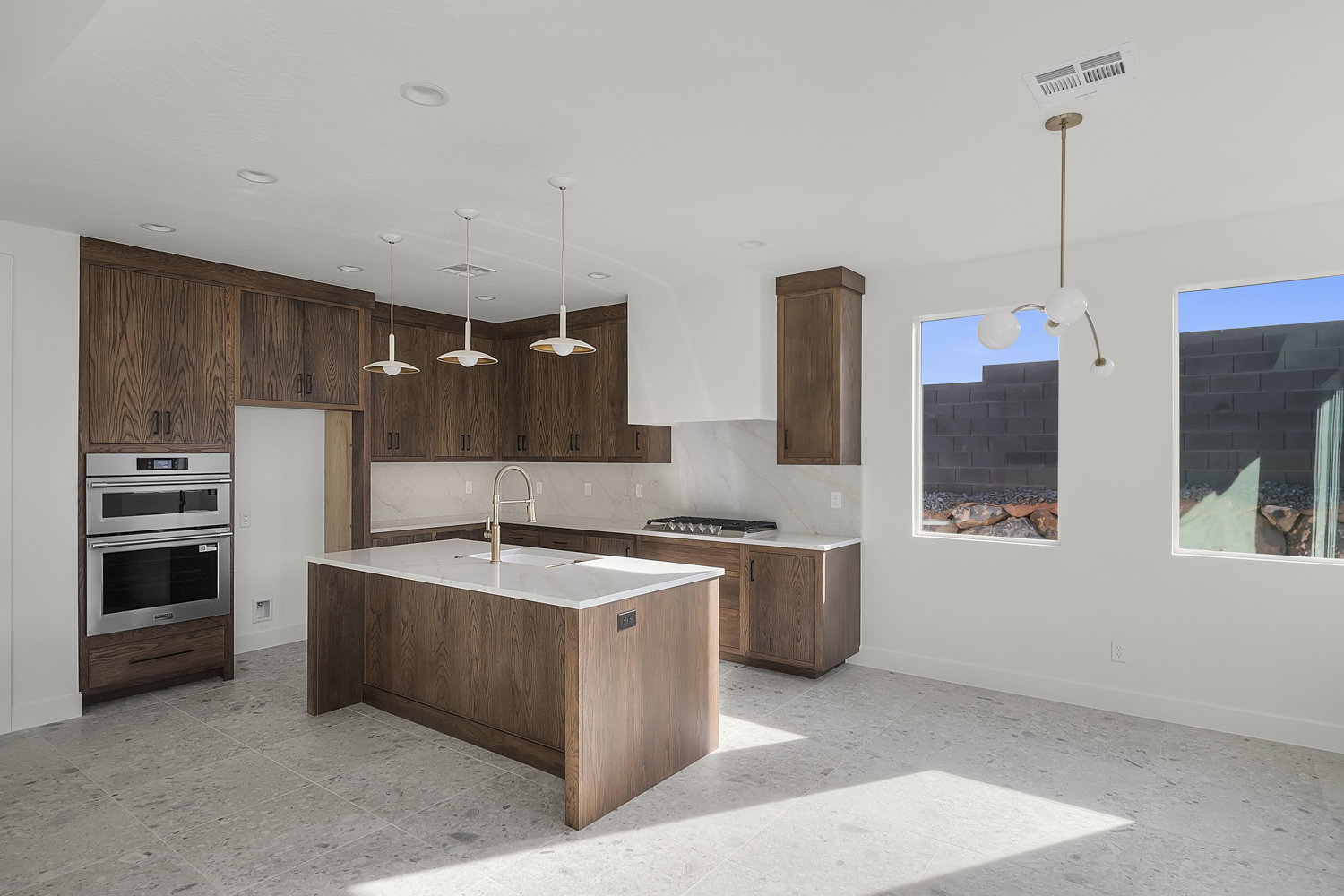 Kitchen with stainless steel appliances, decorative light fixtures, a kitchen island with sink, light stone counters, and decorative backsplash