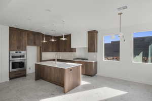 Kitchen with stainless steel appliances, decorative light fixtures, a kitchen island with sink, light stone counters, and decorative backsplash