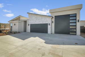 Contemporary home with concrete driveway, a garage, stucco siding, and stone siding