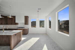 Kitchen featuring light stone countertops, tasteful backsplash, pendant lighting, stainless steel gas stovetop, and dark wood finish cabinetry
