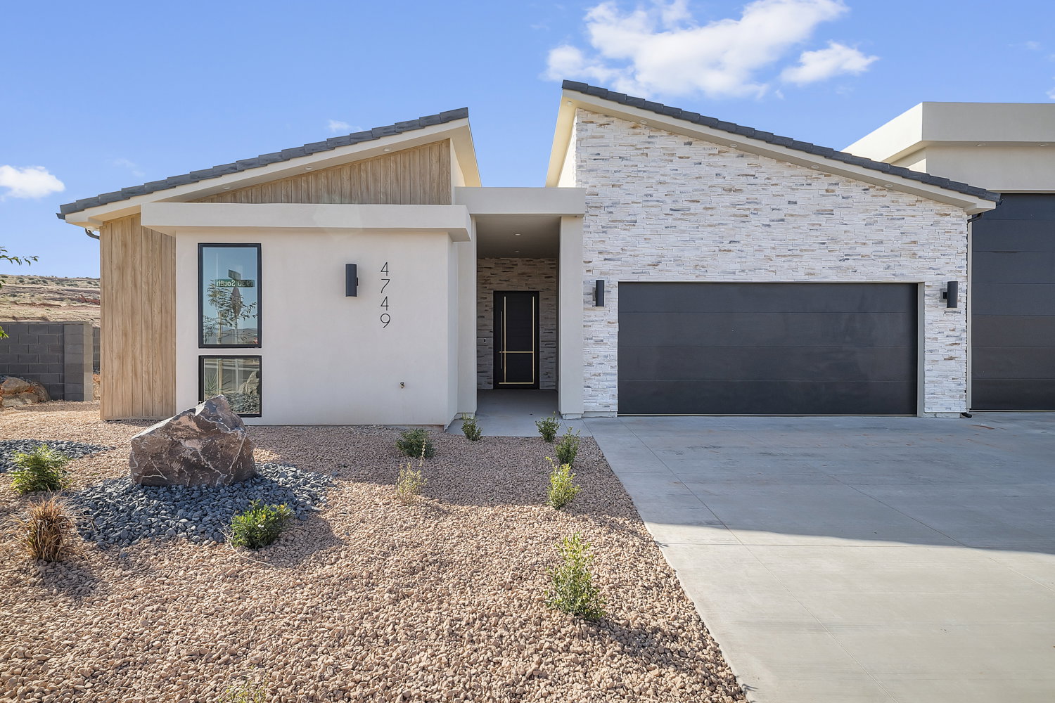 Contemporary home with an attached garage, driveway, and stone siding