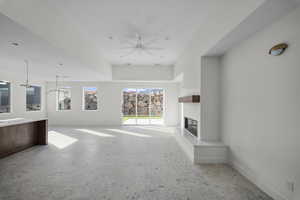 Unfurnished living room with plenty of natural light, a glass covered fireplace, and ceiling fan