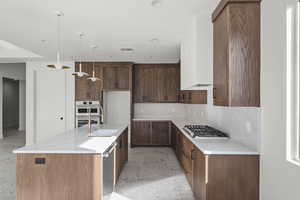 Kitchen featuring a kitchen island with sink, light stone countertops, decorative light fixtures, and backsplash