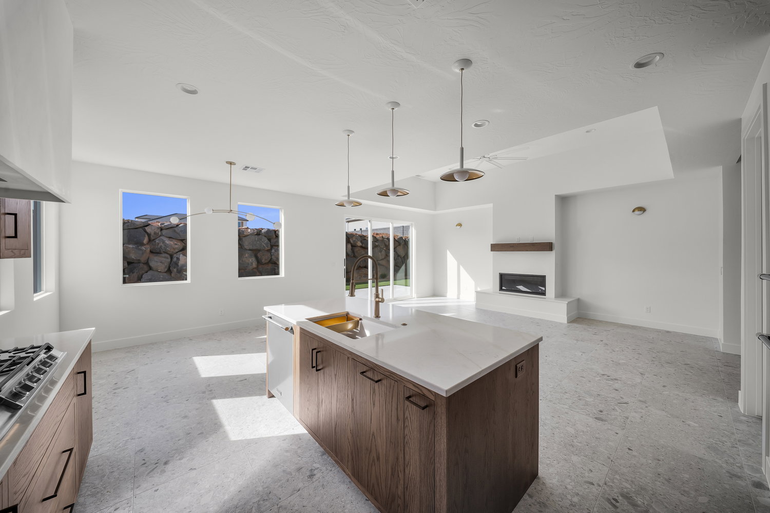 Kitchen featuring open floor plan, an island with sink, a glass covered fireplace, pendant lighting, and light stone counters