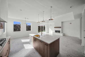 Kitchen featuring open floor plan, an island with sink, a glass covered fireplace, pendant lighting, and light stone counters