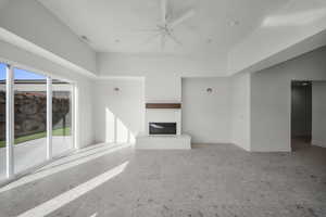 Unfurnished living room featuring ceiling fan, a glass covered fireplace, and a high ceiling