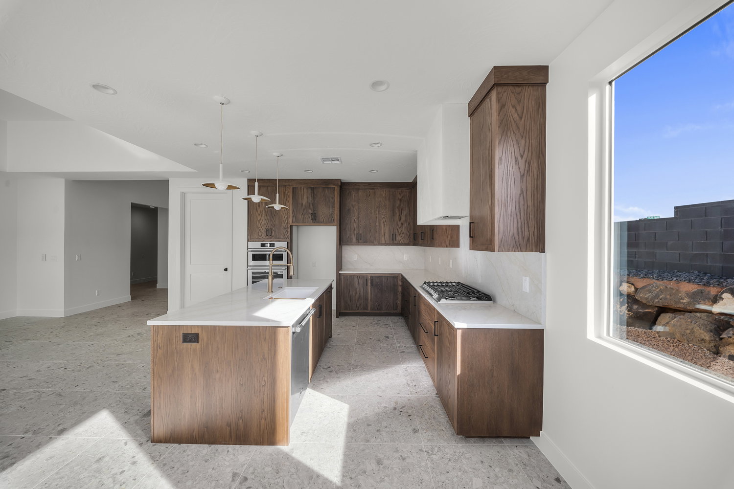 Kitchen featuring an island with sink, light stone counters, hanging light fixtures, stainless steel appliances, and decorative backsplash