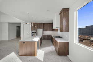 Kitchen featuring an island with sink, light stone counters, hanging light fixtures, stainless steel appliances, and decorative backsplash