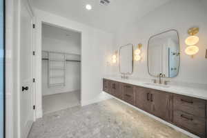 Bathroom featuring a walk in closet, double vanity, and recessed lighting