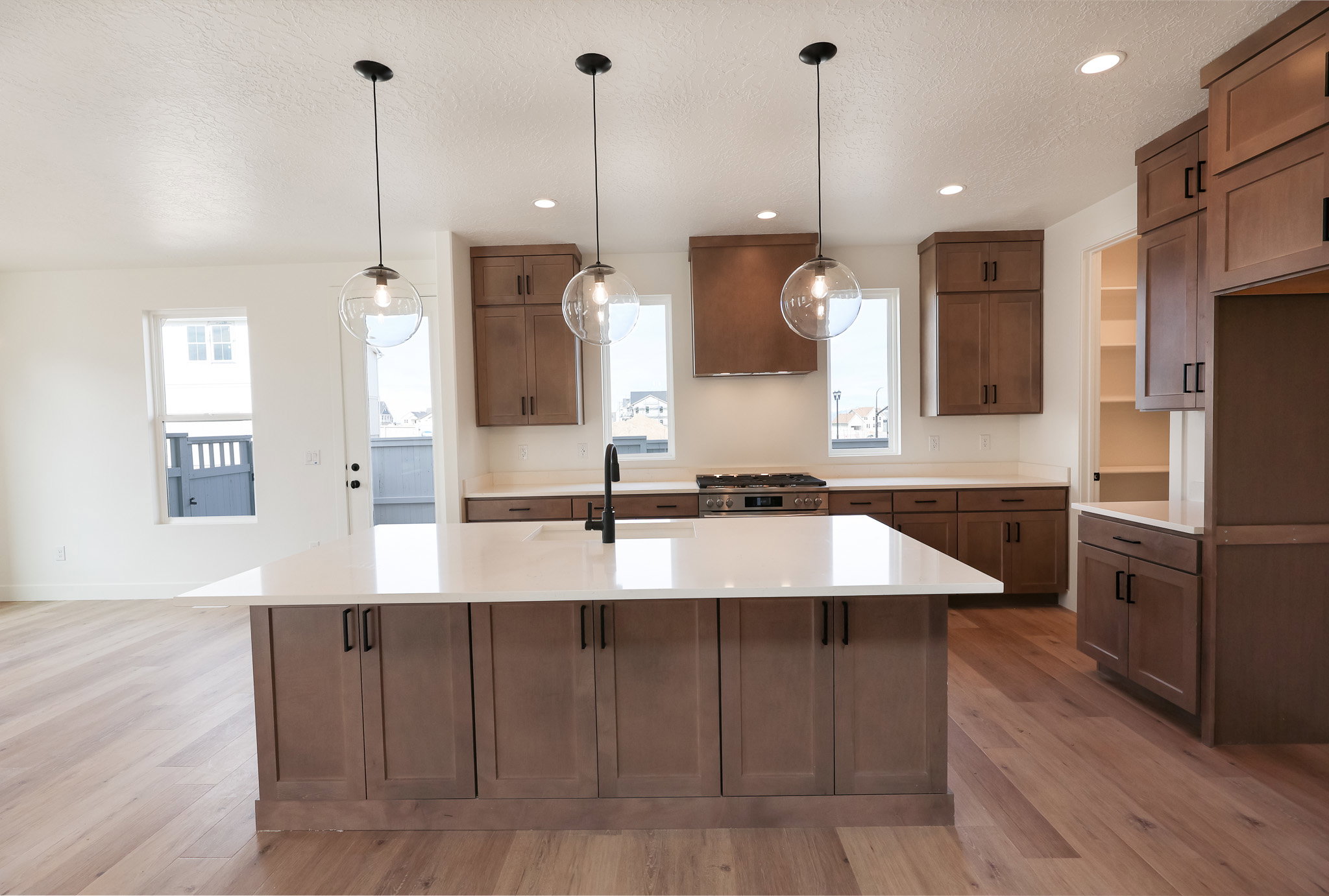 Kitchen featuring light wood finished floors, an island with sink, gas range, exhaust hood, and a textured ceiling