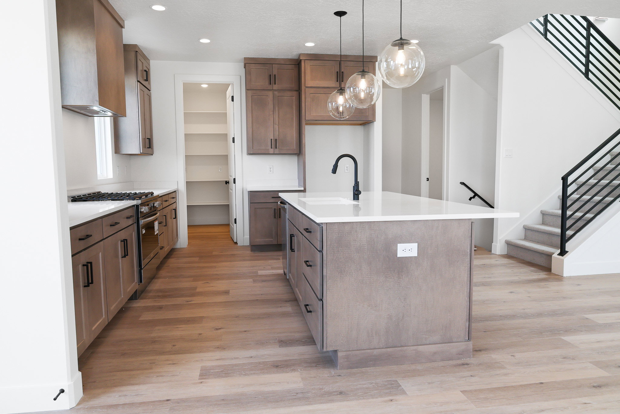 Kitchen featuring stainless steel range with gas cooktop, an island with sink, light stone counters, light wood finished floors, and pendant lighting