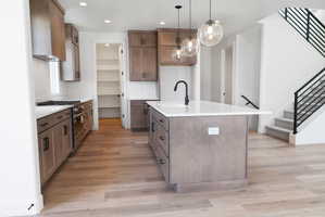 Kitchen featuring stainless steel range with gas cooktop, an island with sink, light stone counters, light wood finished floors, and pendant lighting