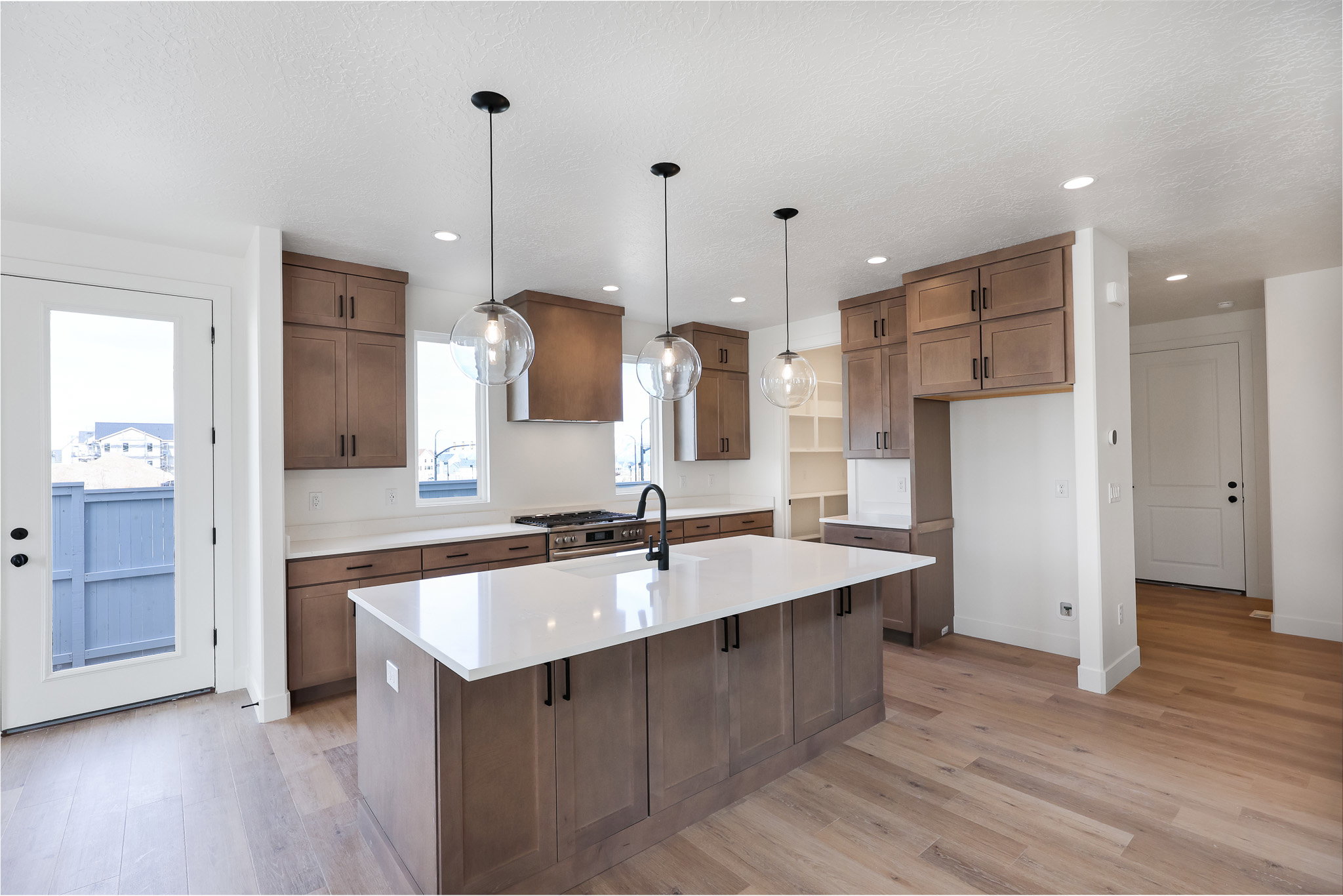 Kitchen with light wood-style flooring, a kitchen island with sink, light stone countertops, stainless steel range with gas cooktop, and wood finish cabinetry