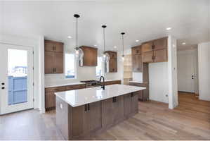 Kitchen with light wood-style flooring, a kitchen island with sink, light stone countertops, stainless steel range with gas cooktop, and wood finish cabinetry