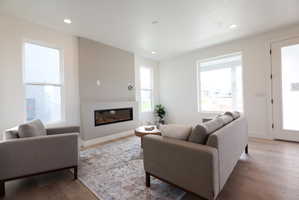 Living room with wood finished floors, a glass covered fireplace, and recessed lighting