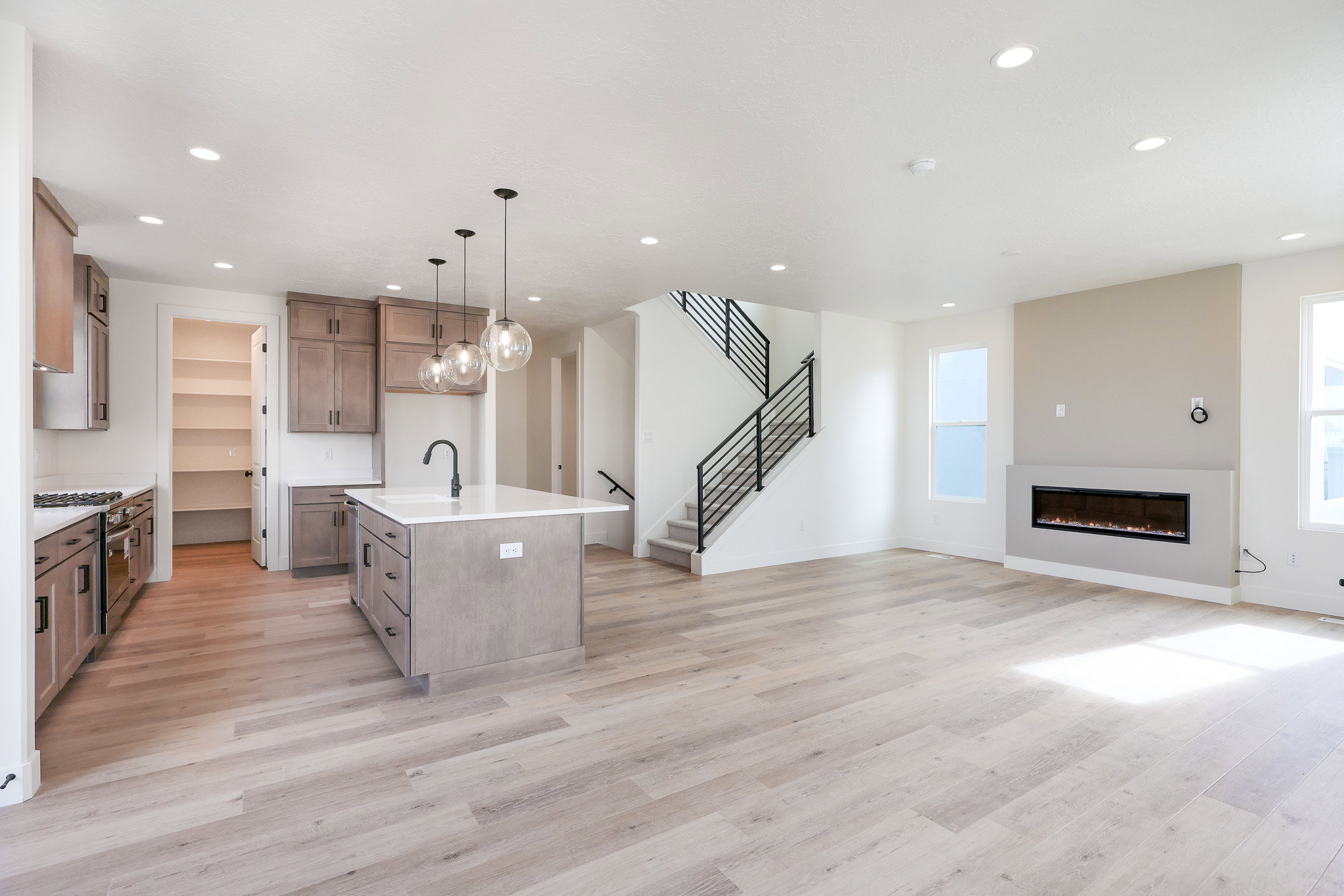 Kitchen with open floor plan, an island with sink, gas range, hanging light fixtures, and light stone counters