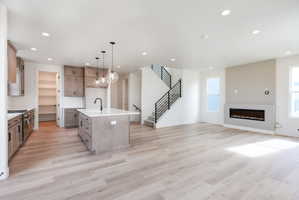 Kitchen with open floor plan, an island with sink, gas range, hanging light fixtures, and light stone counters