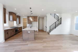 Kitchen with gas stove, light wood finished floors, an island with sink, light stone countertops, and wood finish cabinets