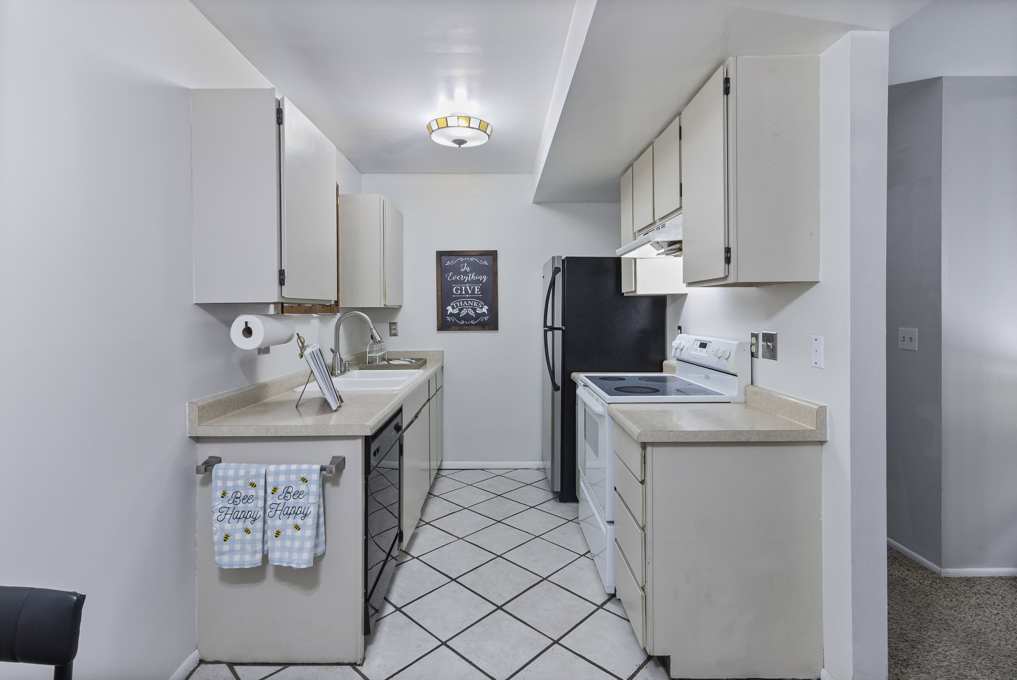 Kitchen featuring light countertops, white electric range oven, light tile patterned floors, black dishwasher, and white cabinetry