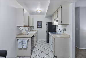 Kitchen featuring light countertops, white electric range oven, light tile patterned floors, black dishwasher, and white cabinetry