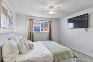 Carpeted bedroom featuring ceiling fan and a textured ceiling