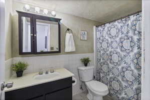 Bathroom with vanity, a shower with shower curtain, tile walls, and wainscoting
