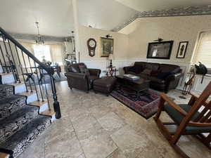 Living room with wallpapered walls, a wainscoted wall, hanging lights, lofted ceiling, and a decorative wall