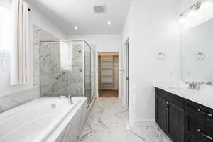 Bathroom with vanity, a walk in closet, a marble finish shower, a bath, and light marble finish floors