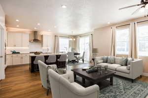 Living room featuring dark wood-style flooring, a chandelier, a ceiling fan, and a textured ceiling