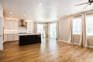 Kitchen with suspended lighting, decorative backsplash, a kitchen island with sink, dark wood-style flooring, and a ceiling fan