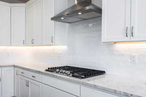 Kitchen with island range hood, white cabinetry, light stone counters, and stainless steel gas stovetop