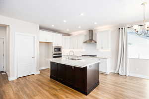 Kitchen with light stone counters, a kitchen island with sink, suspended lighting, light wood-style flooring, and two tone cabinets