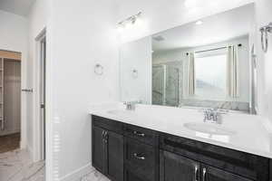 Bathroom featuring double vanity, light marble finish floors, a marble finish shower, and a spacious closet