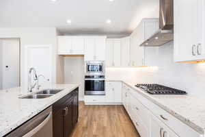 Kitchen featuring stainless steel appliances, light stone counters, dual tone cabinets, light wood-style flooring, and backsplash