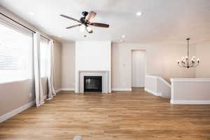 Unfurnished living room with light wood finished floors, ceiling fan, a glass covered fireplace, and hanging lights