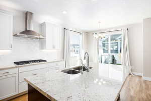 Kitchen featuring light wood finished floors, a chandelier, a kitchen island with sink, white cabinetry, and a textured ceiling