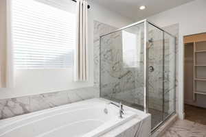 Bathroom featuring a marble finish shower, a garden tub, marble look tile flooring, a spacious closet, and recessed lighting