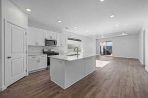 Kitchen with stainless steel appliances, white cabinetry, a kitchen island with sink, dark wood-type flooring, and recessed lighting
